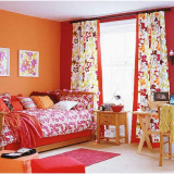 Dormitor amenajat foarte colorat cu perdele inflorate si peretii portocalii