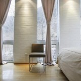 Dormitor cu perete placat cu caramida alba si fasii de draperii din bumbac crem simplu