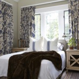 Dormitor amenajat in stil rustic cu mobilier crem si perdele alb mudar cu flori albastru aprins